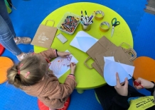Dzieci przy zielonym stoliczku, kolorują papierowe krople i papierowe torby.
