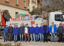 16 osób stoi przed ciężarówką załadowaną darami dla Ukrainy.