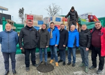 8 osób stoi przed ciężarówką załadowaną darami dla Ukrainy.