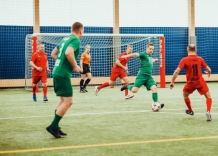 Piłkarze w czerwonych i zielonych strojach kopią piłkę.