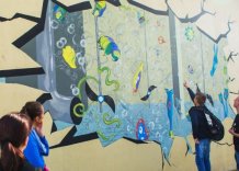 Młodzież wskazuje na kolorowy mural umieszczony na ścianie jednego z reaktorów oczyszczalni ścieków Płaszów. 